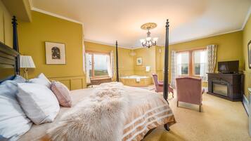 A bedroom with a four-poster bed, a sitting area with a chair and a fireplace, and a view of the outdoors through a window.