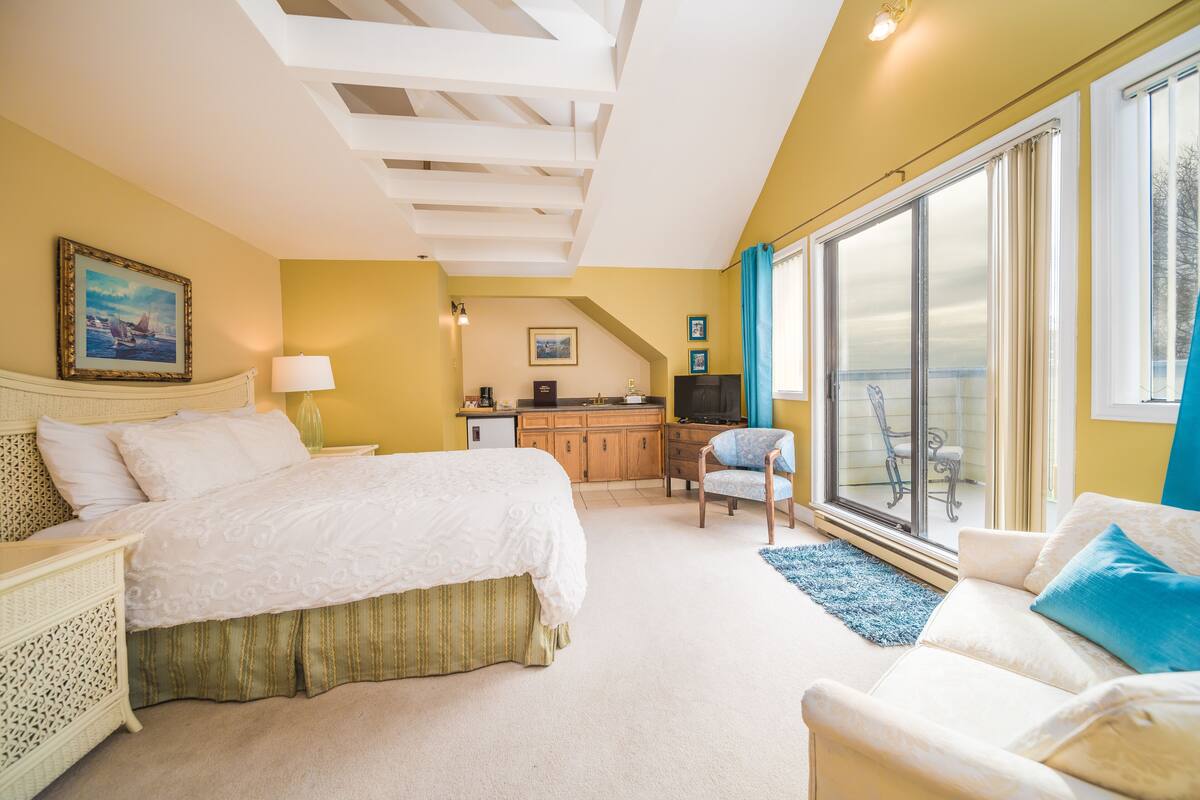 A bedroom with a bed, a desk, a chair, and a view of the outdoors.
