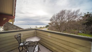 Un balcon avec une table et des chaises, donnant sur une étendue d’eau et des arbres.