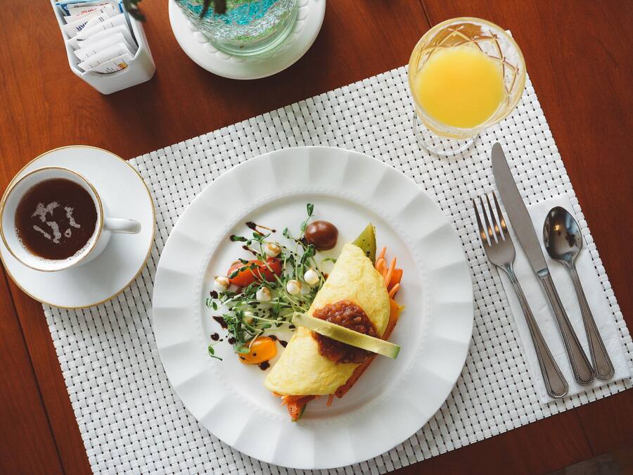 A breakfast setting with a plate of food, a cup of coffee, and a glass of orange juice on a wooden table.