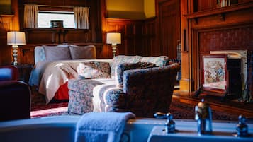 Una habitación tradicional con una cama, dos sillones con estampado, una chimenea y un espejo grande.