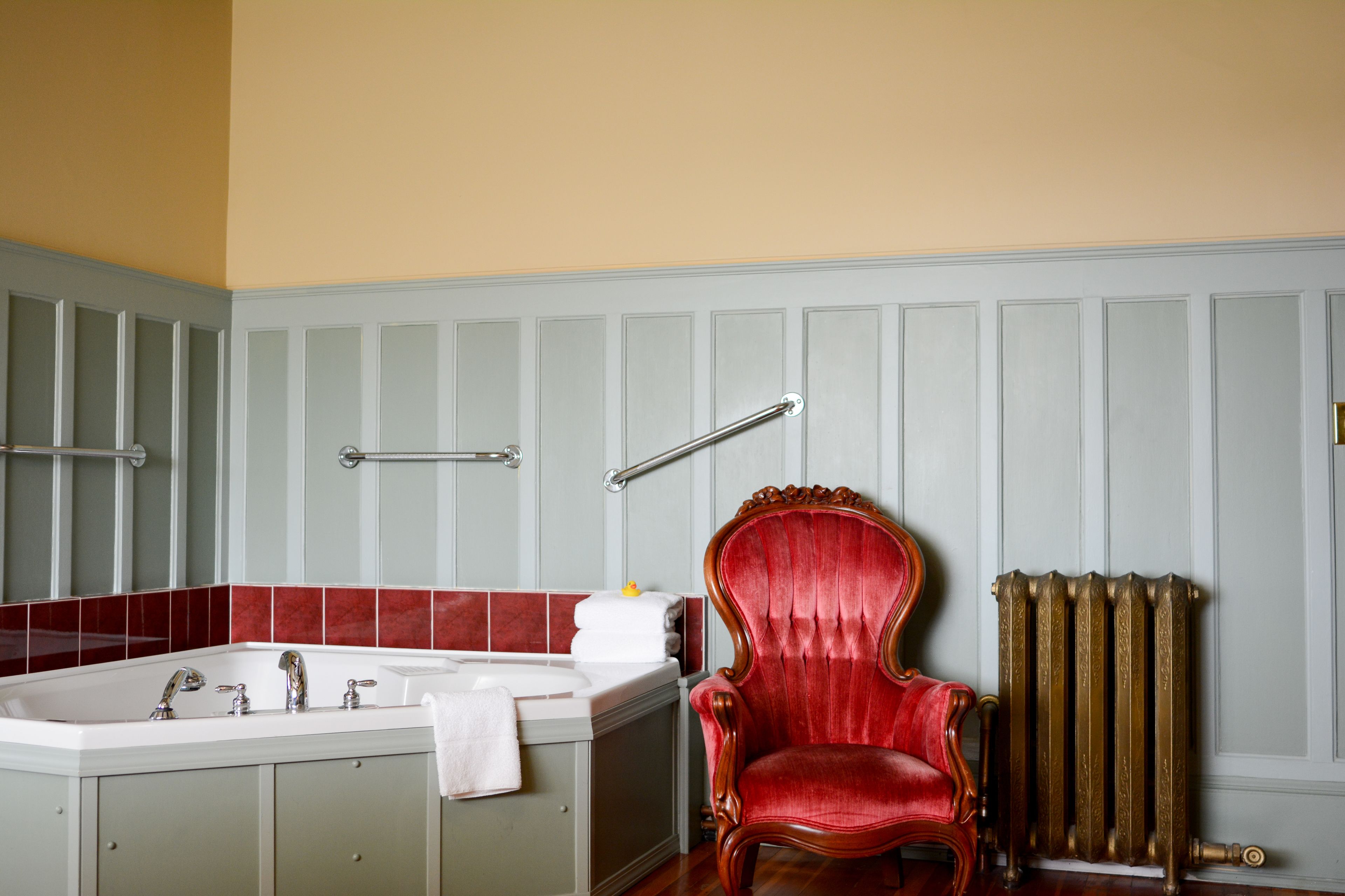 A bathroom with a bathtub, a red chair, and a radiator.