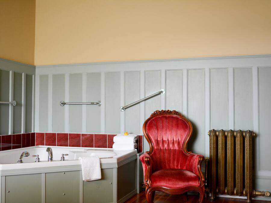 A bathroom with a bathtub, a red chair, and a radiator.