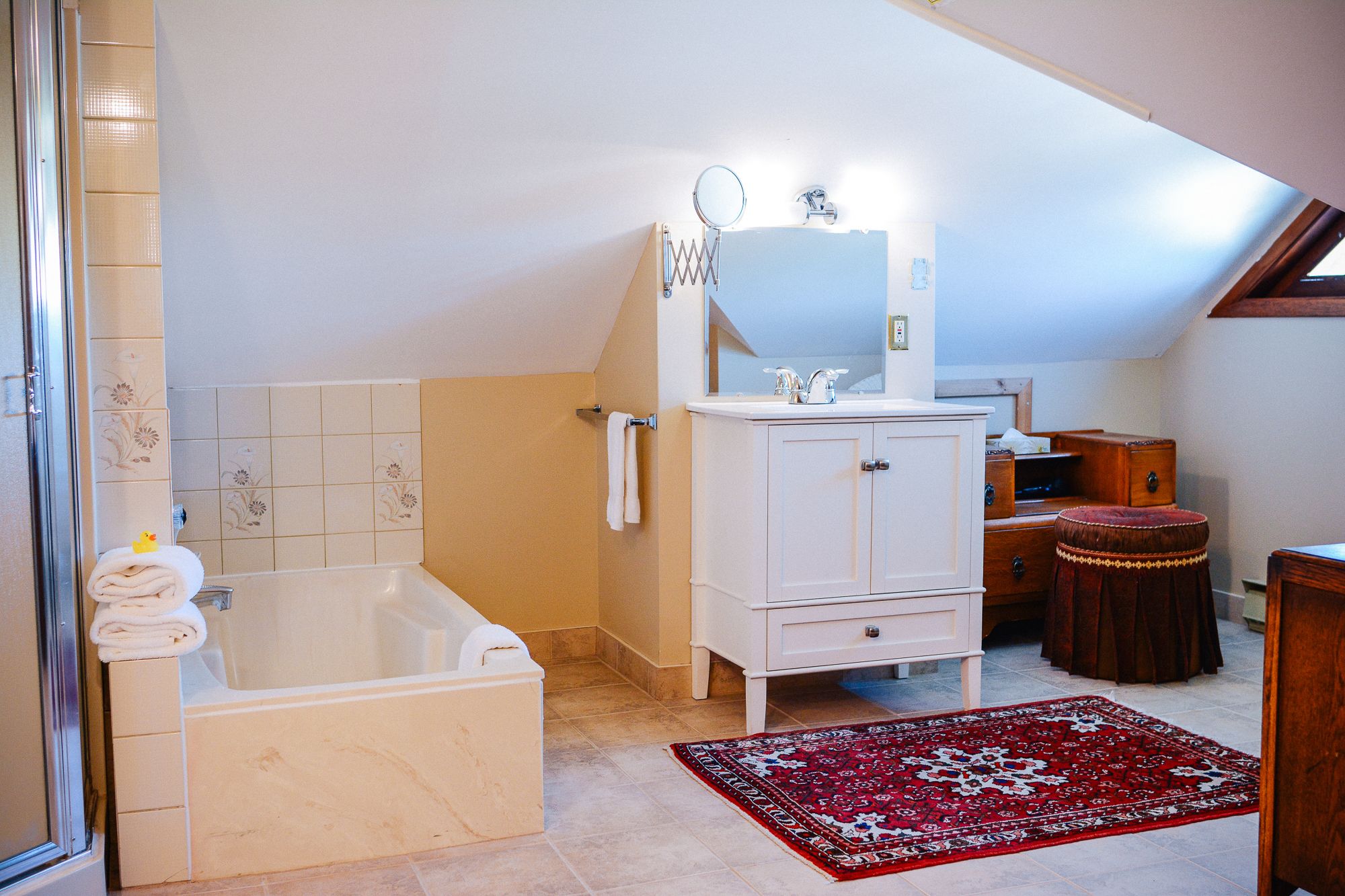 Une salle de bain avec une baignoire, un meuble-lavabo avec un miroir et un tapis rouge à motifs.