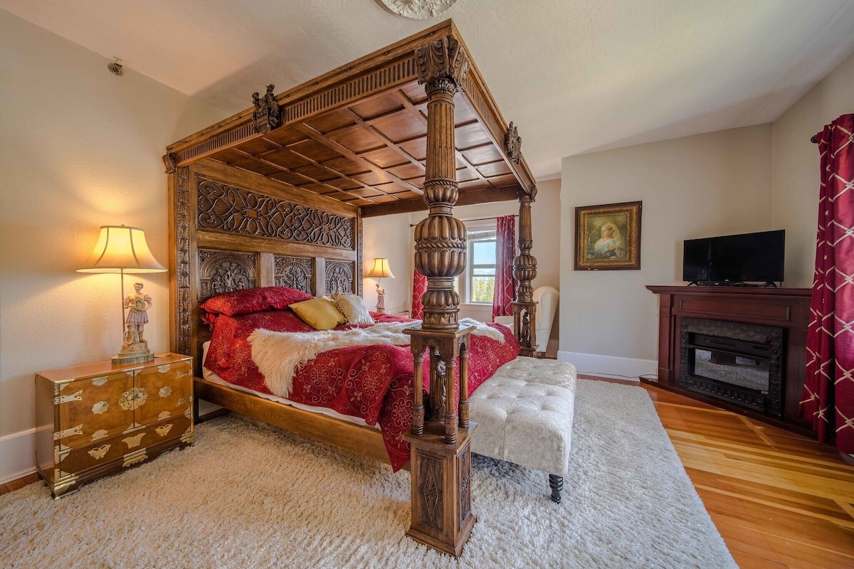 A four-poster bed with a wooden canopy, a red and white bedspread, and a white upholstered bench.