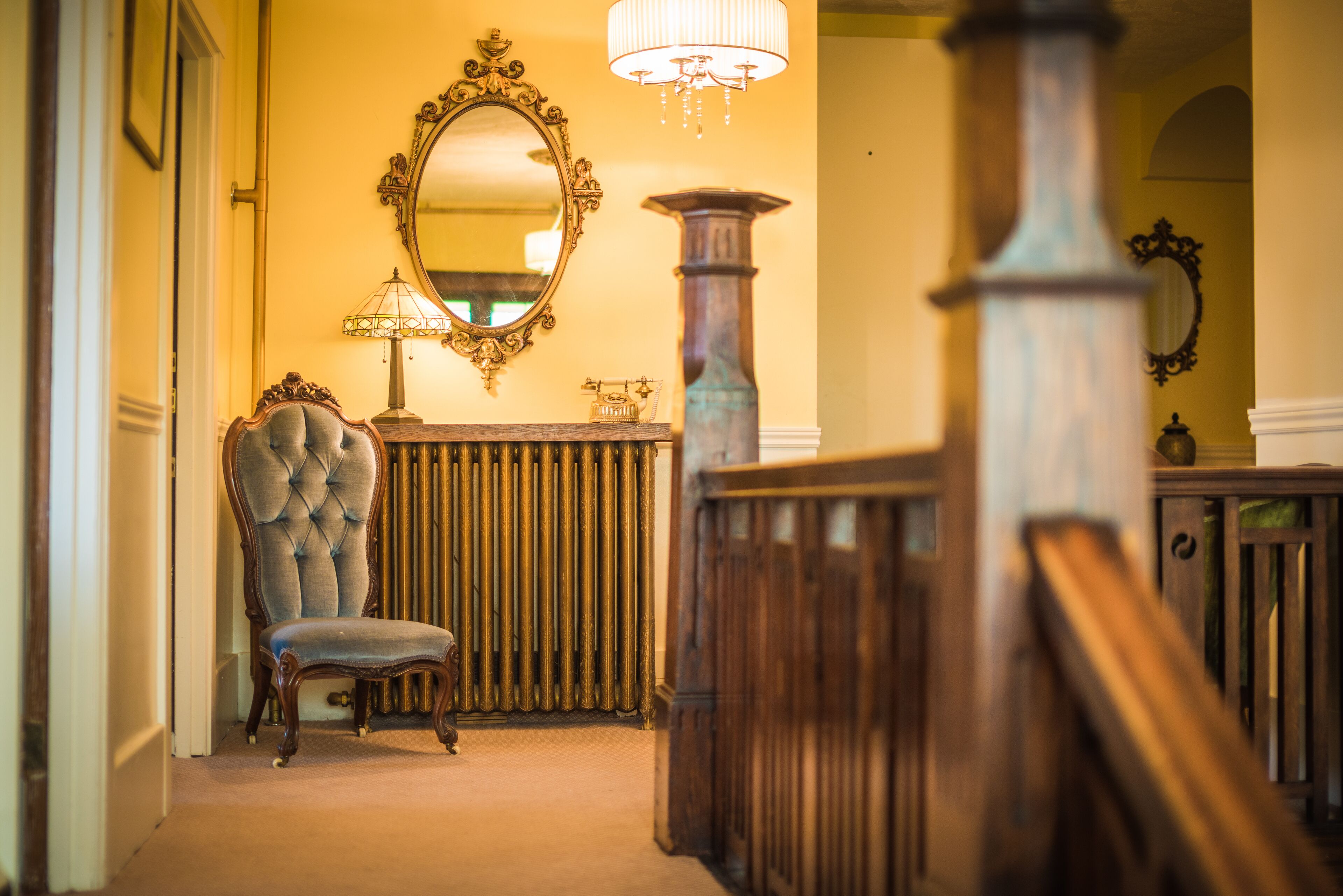 A grand hallway with a large mirror, a tufted chair, and a wooden staircase.