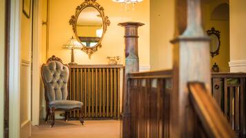 A grand hallway with a large mirror, a tufted chair, and a wooden staircase.