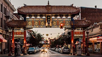 A traditional Chinese gate with intricate designs and characters, leading to a street lined with parked cars and buildings.