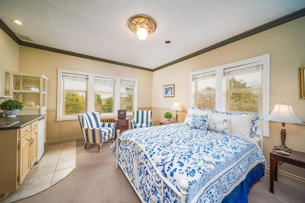 A bedroom with a large bed, a chair, a desk, and a window.