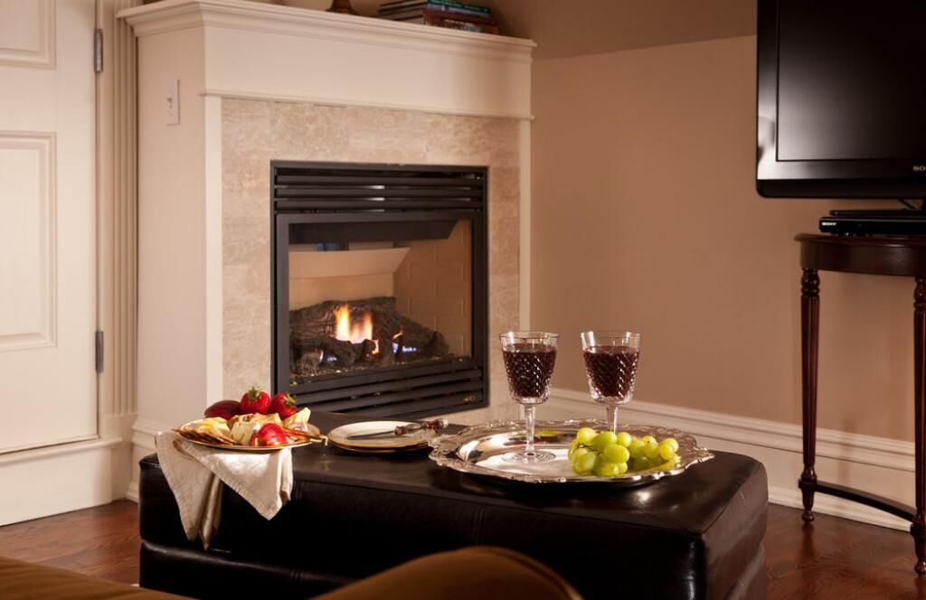 A cozy room with a fireplace, a television, and a table set with fruits and glasses.