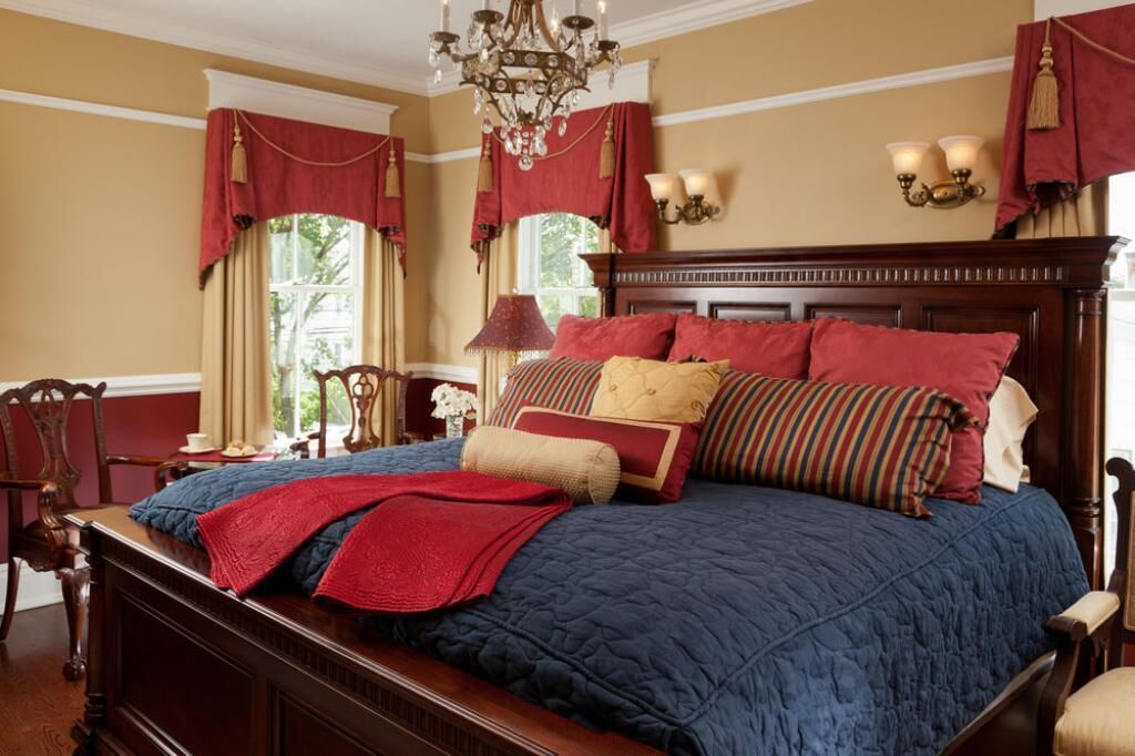 A large bed with a wooden headboard, red and blue bedding, and multiple pillows.