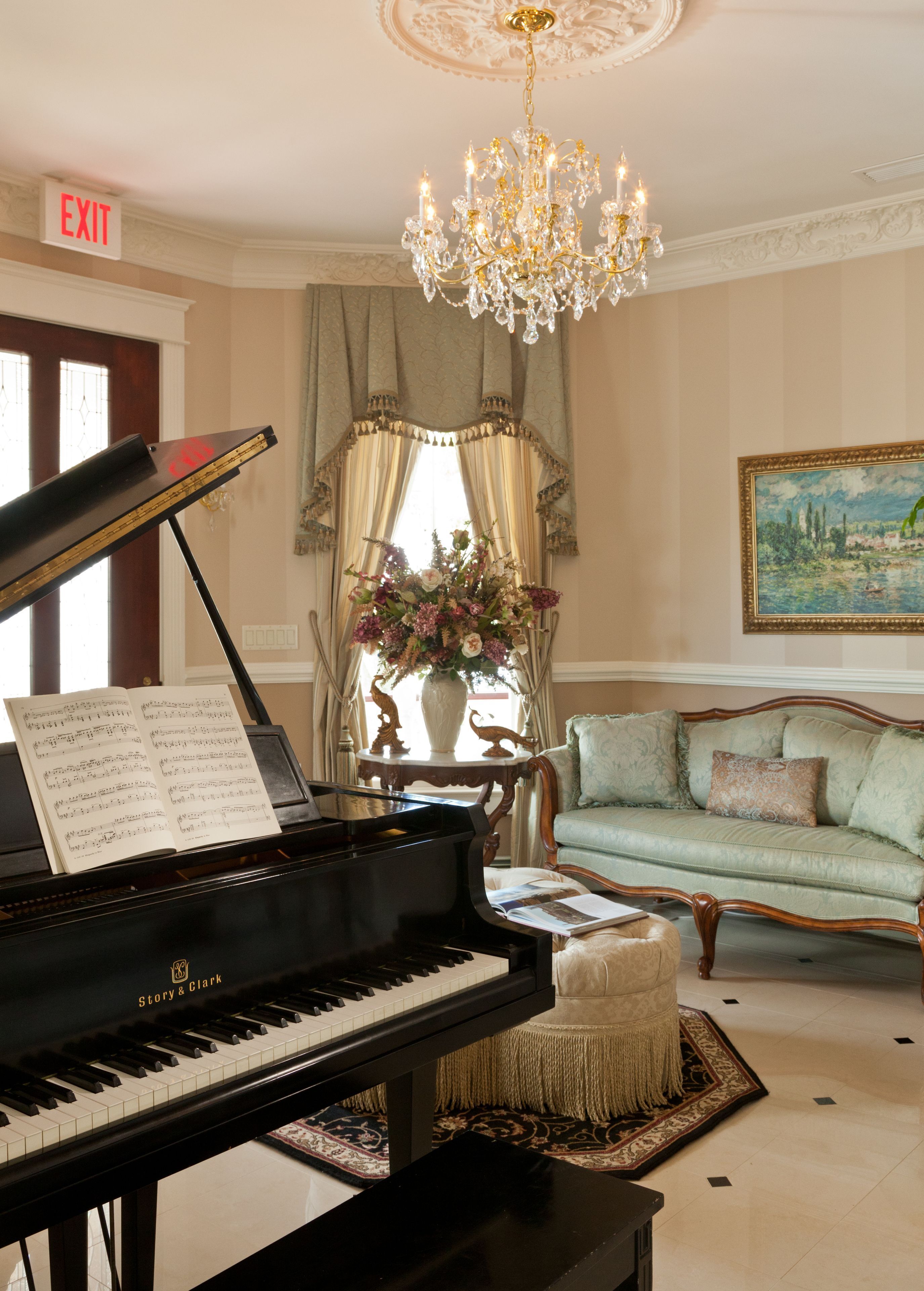 A grand piano with sheet music, a chandelier, a sofa, and a painting in a well-lit room.