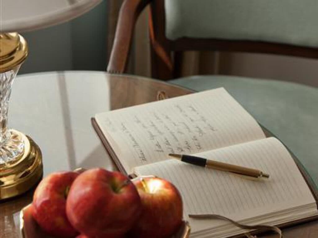 A table with an open notebook, a pen, and a few apples.