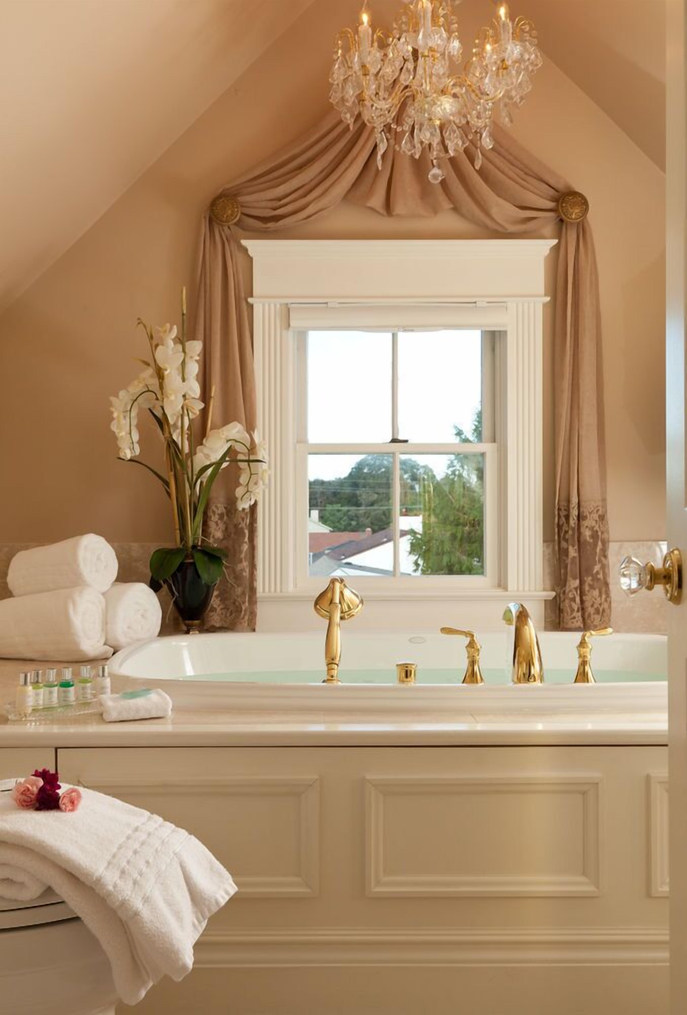 A bathroom with a large bathtub, a chandelier, and a window with curtains.
