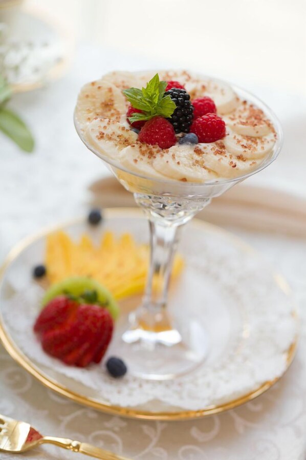 Un dessert servi dans un verre à martini, garni de fruits rouges et d’une feuille de menthe, présenté sur une assiette blanche à bord doré.