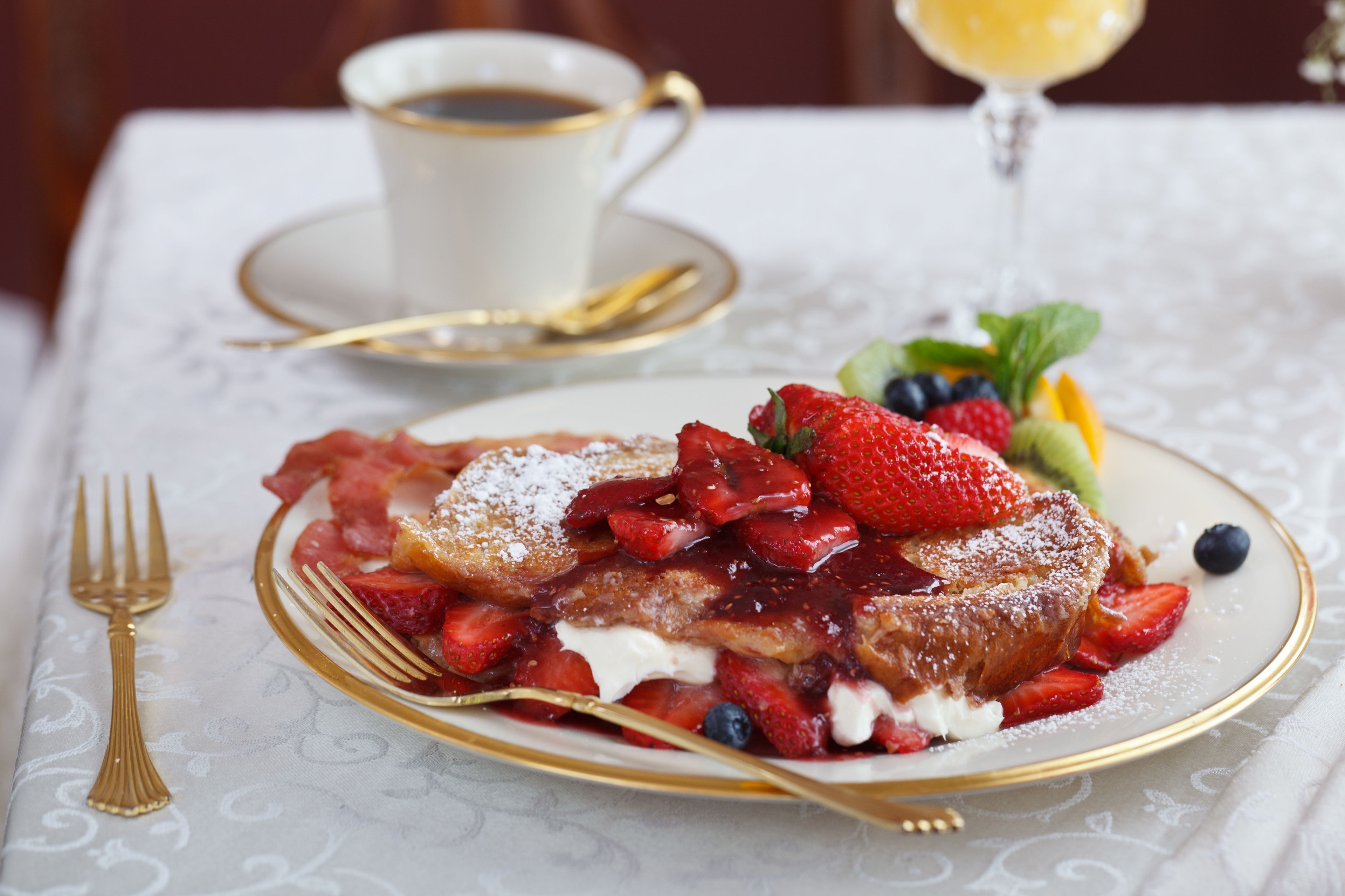 A plate of French toast with strawberries and blueberries, a cup of coffee, and a glass of orange juice on a table.