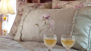A bed with a floral-patterned bedspread, two glasses of white wine on a tray, and a lace headboard.