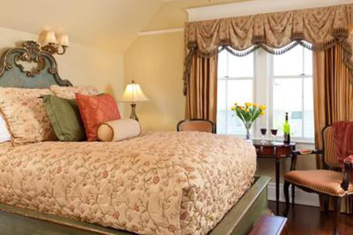 A hotel room with a large bed, a desk with a lamp, and a chair.