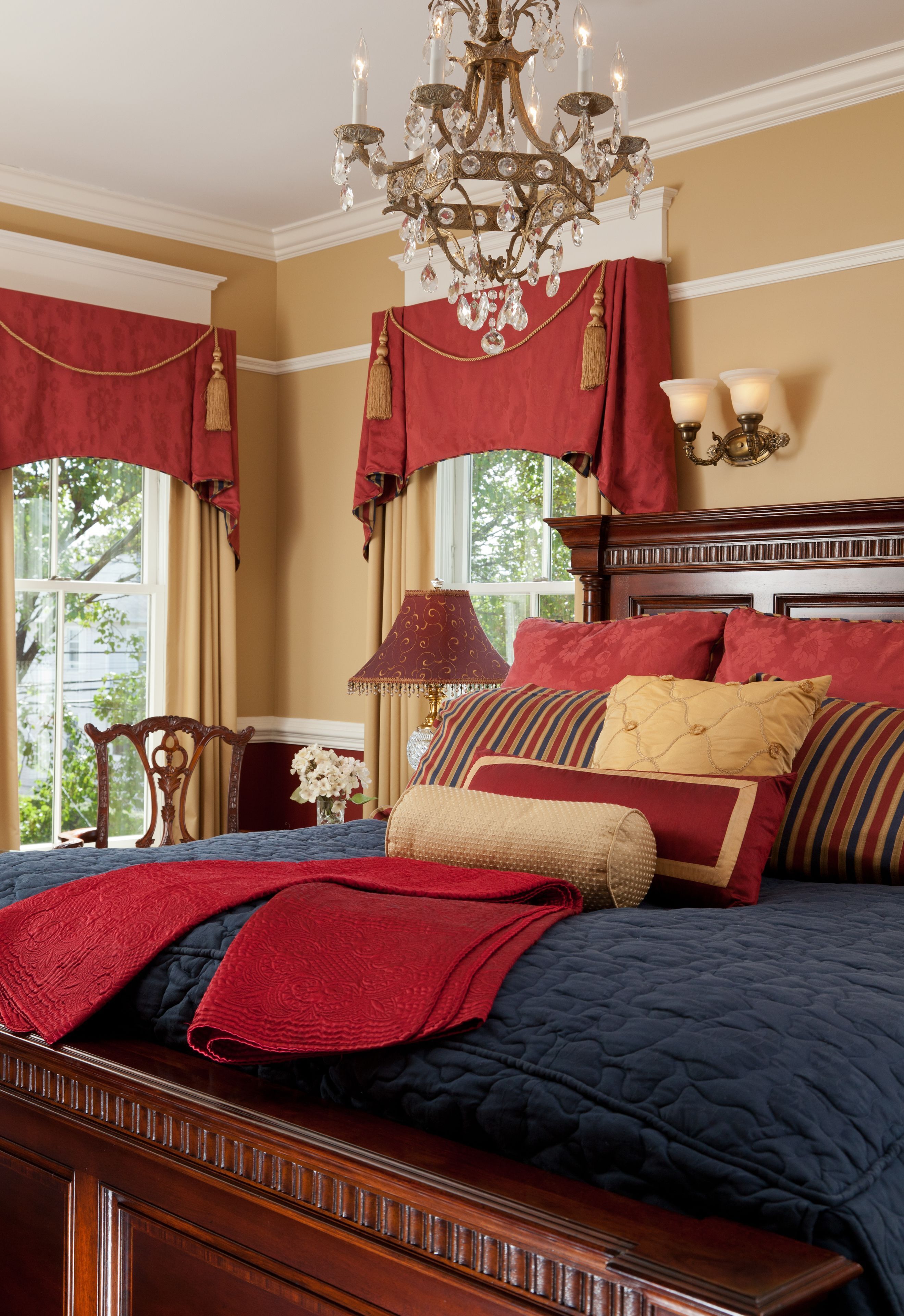 Un dormitorio con una cama grande, cortinas rojas, un candelabro y una ventana con vistas a árboles.