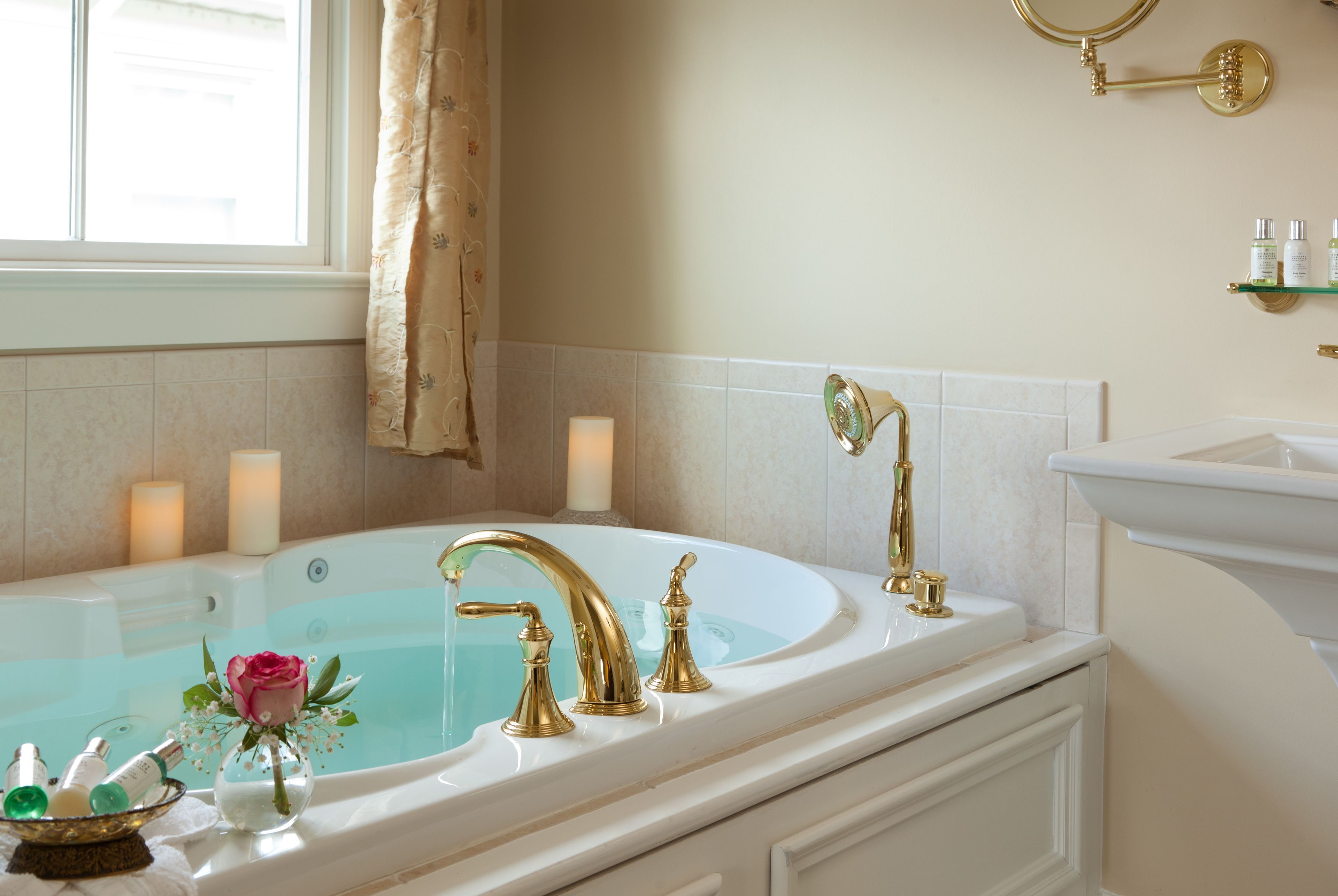 A bathroom with a large bathtub, a gold faucet, and a vase with a pink rose.