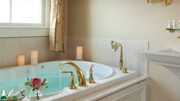 Une salle de bain avec une grande baignoire, un robinet doré et un vase contenant une rose rose.
