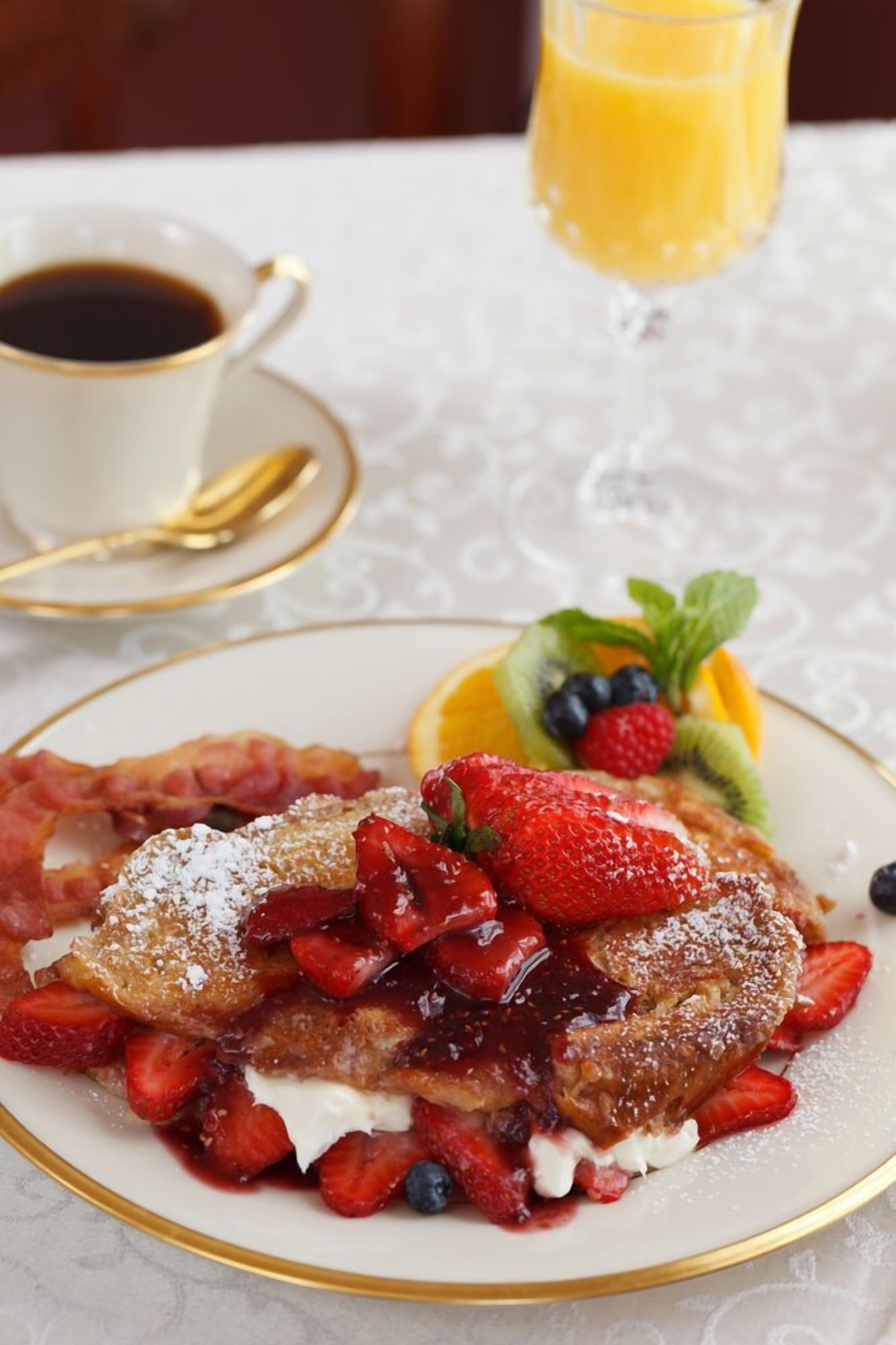 A plate of French toast with strawberries and blueberries, a glass of orange juice, and a cup of coffee on a table.