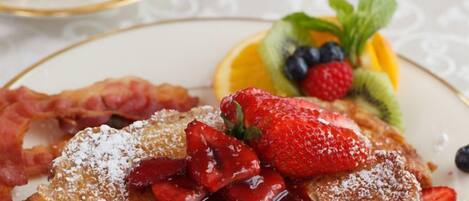 A plate of French toast with strawberries and blueberries, a glass of orange juice, and a cup of coffee on a table.