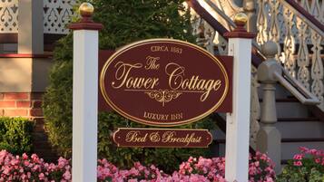 A sign for The Tower Cottage, a luxury inn with a bed and breakfast, featuring a classic architectural style with a porch and decorative railings.