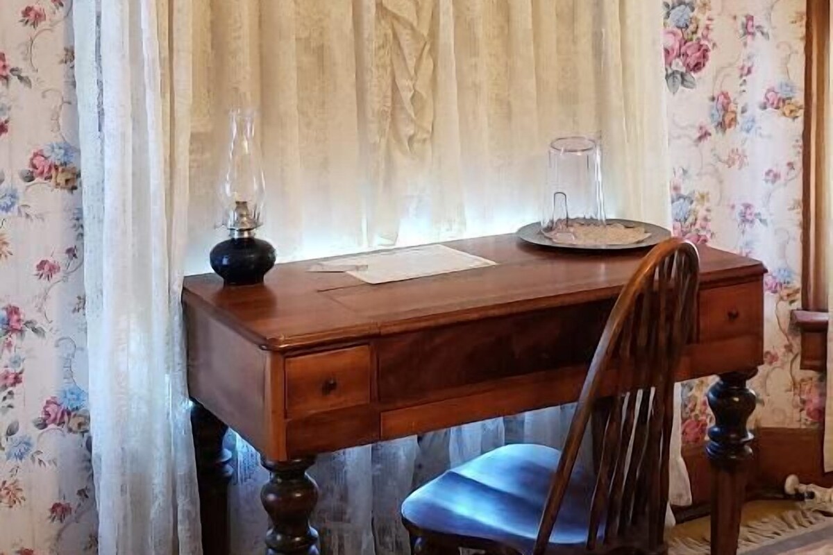 Een houten bureau met een stoel, een lamp en een glas op het bureau.