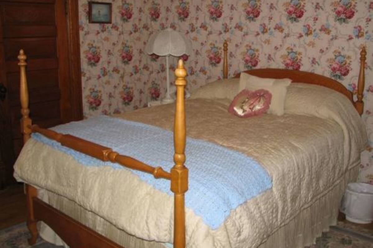 Une chambre à coucher avec un lit à baldaquin en bois, un papier peint à motifs floraux et un plaid bleu.