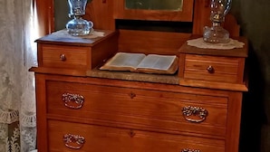 Un aparador de madera con un espejo, dos floreros de vidrio y un libro abierto.