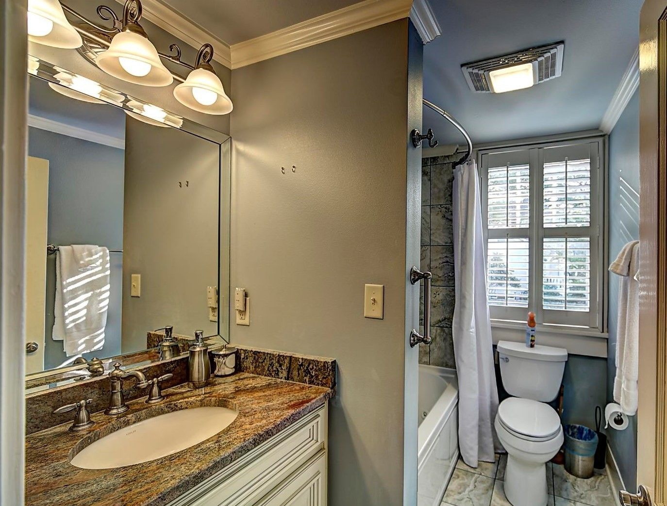 A bathroom with a granite countertop sink, a large mirror, and a shower area with a window.