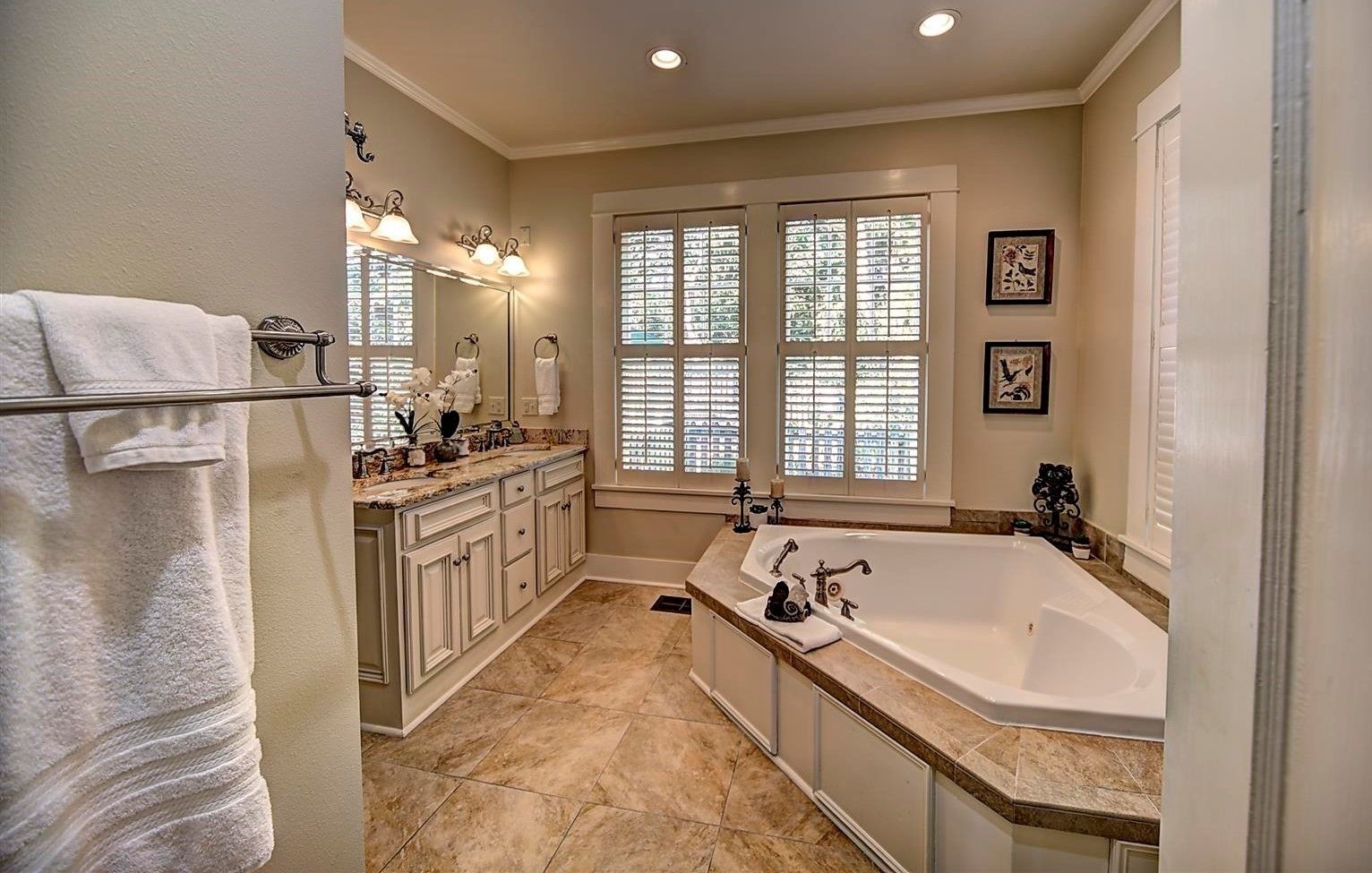 A spacious bathroom with a large bathtub, double vanity with a mirror, and a window with blinds.