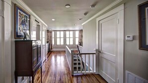 A hallway with wooden flooring, white walls, and a staircase leading to another level. - The Good House B&B (Natchitoches)