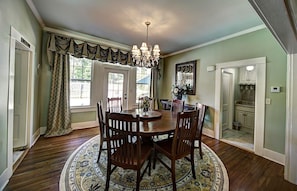 A dining room with a wooden table and chairs, a chandelier, and a patterned rug. - The Good House B&B (Natchitoches)