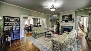 A spacious living room with a fireplace, a staircase, and a dining area. - The Good House B&B (Natchitoches)