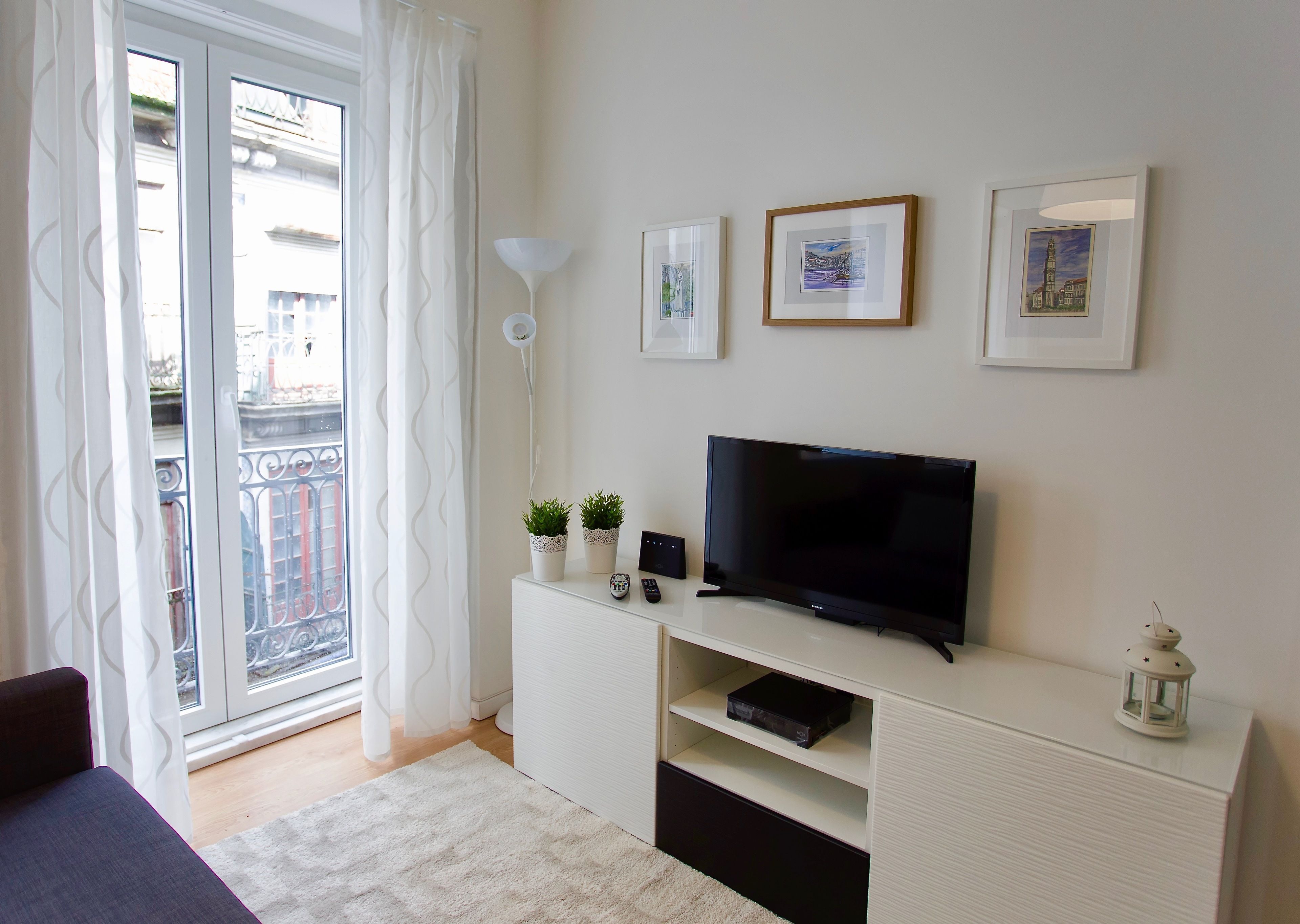 Un salon moderne doté d’un téléviseur à écran plat, d’un meuble de rangement blanc et d’un balcon offrant une vue sur les immebles.