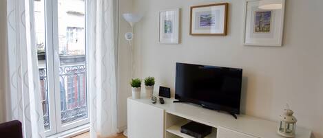 Un salon moderne doté d’un téléviseur à écran plat, d’un meuble de rangement blanc et d’un balcon offrant une vue sur les immebles.