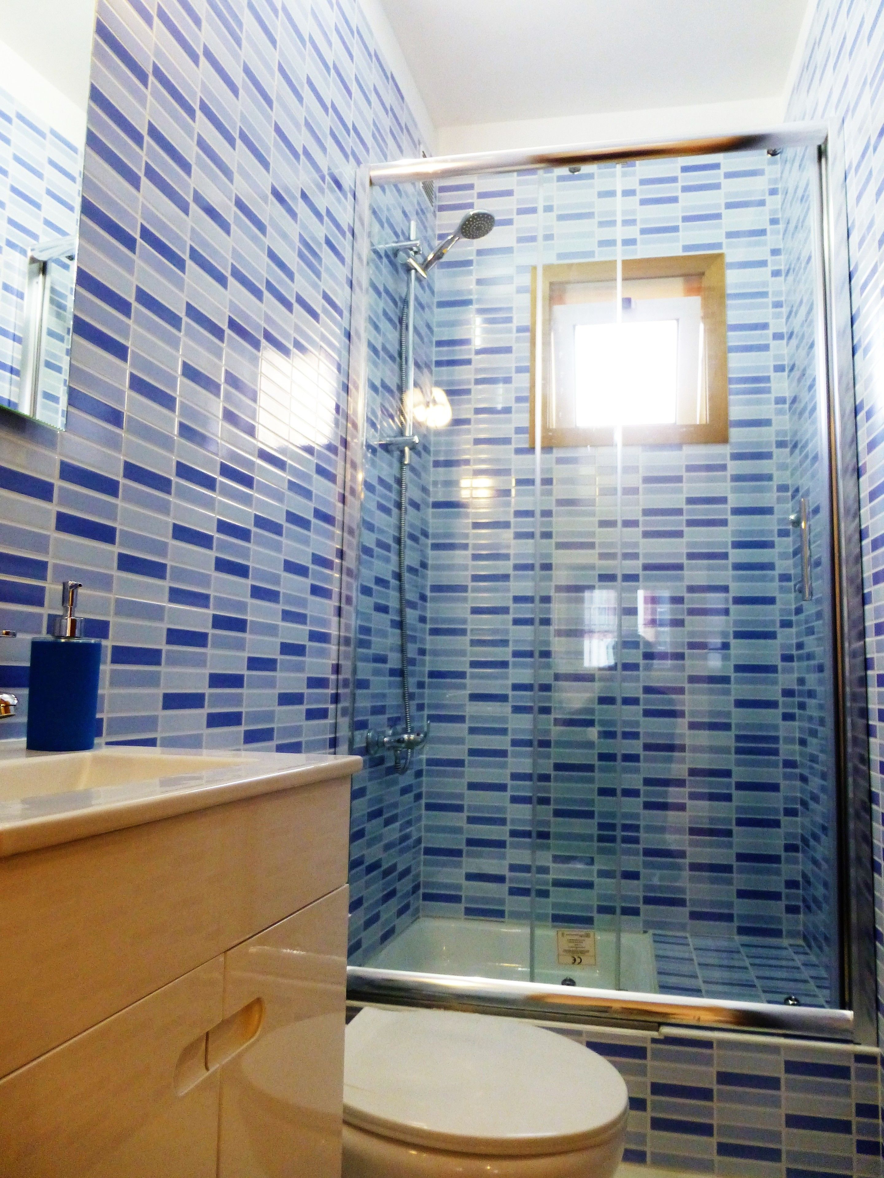Ein Badezimmer mit Duschkabine, Toilette und Waschbecken mit blauem Seifenspender.