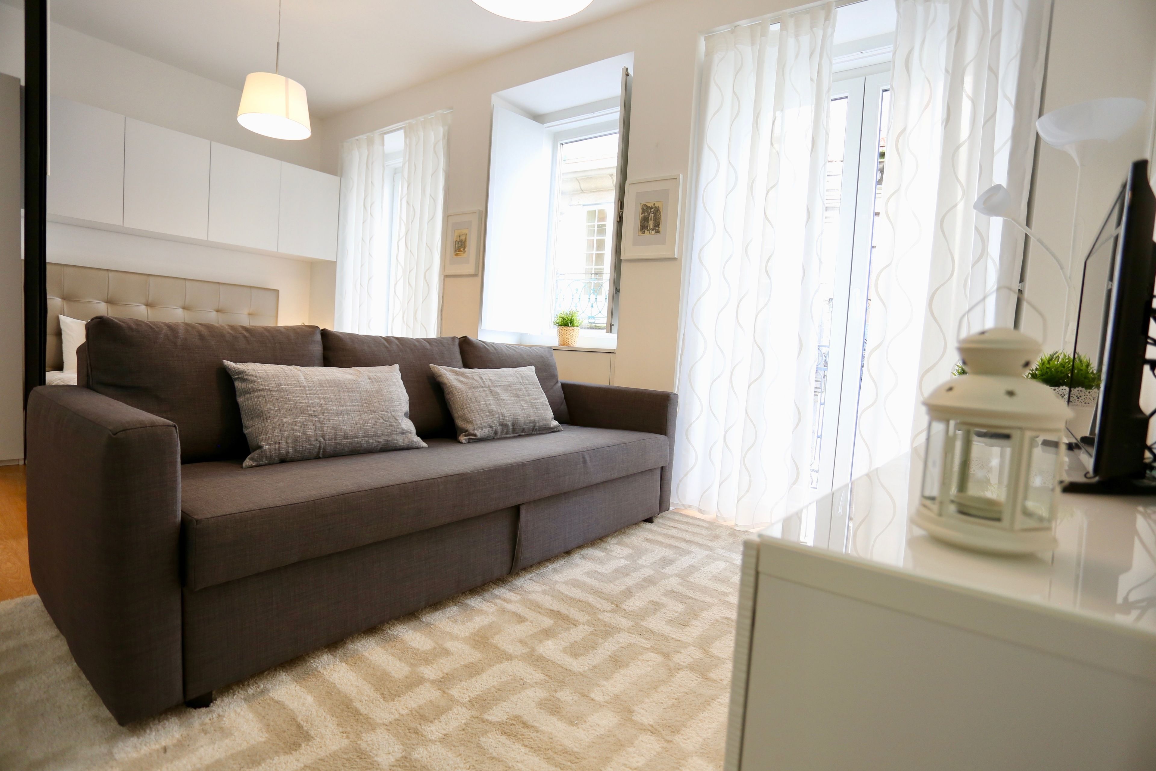 A modern living room with a grey sofa, a white rug, and a small table with a lantern.