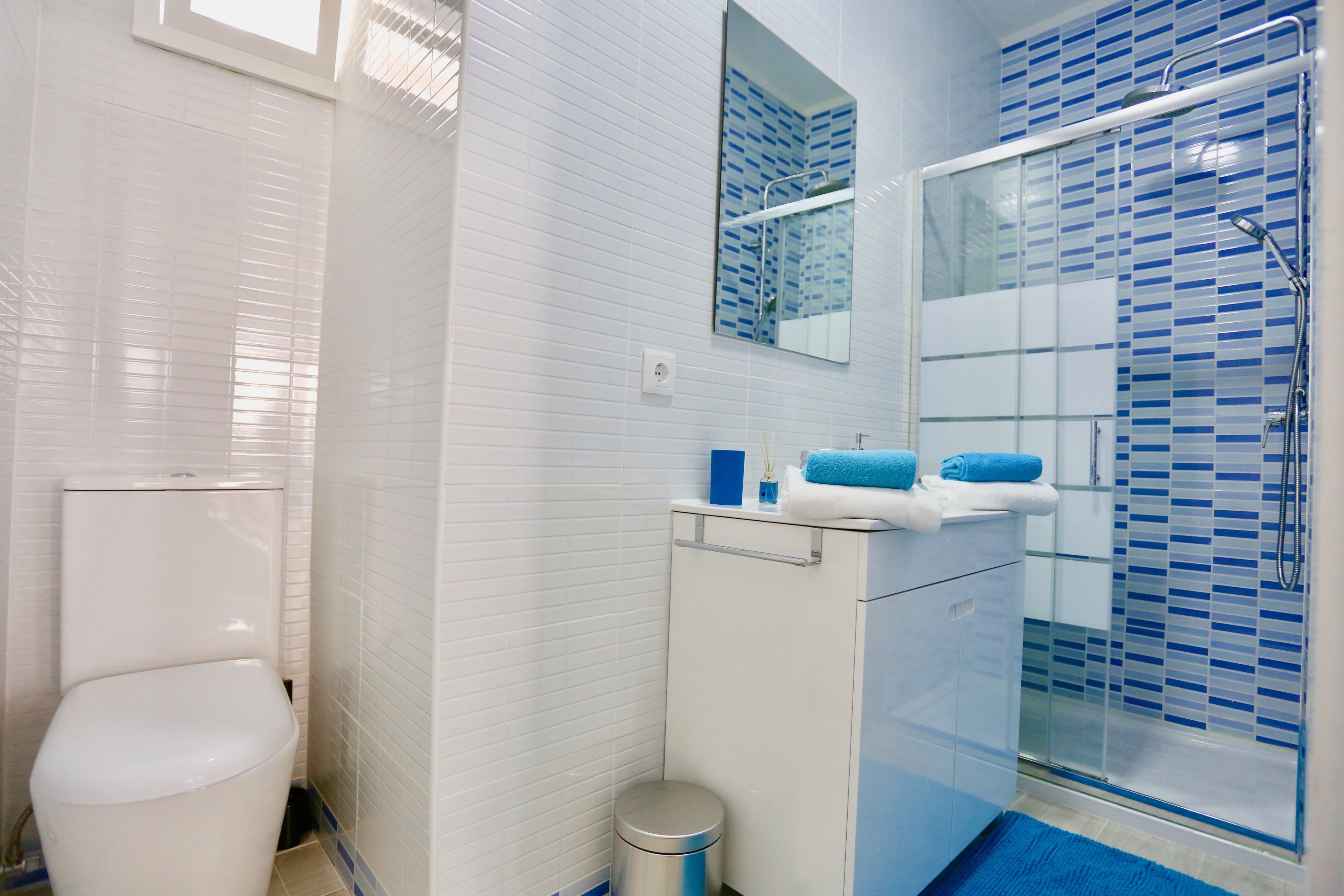 Ein modernes Badezimmer mit Toilette, einem Waschbecken mit Spiegel und einer Duschkabine mit blauen Fliesen.