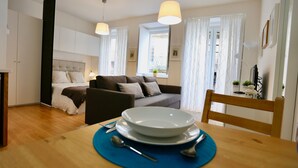 A modern living room with a sofa, a dining table with plates and cutlery, and a bed with a headboard. - D&S - Porto São Bento Apartment II (Porto)