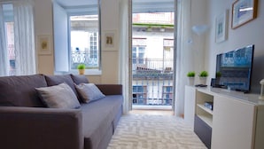 A modern living room with a sofa, a TV, and a balcony with a metal railing. - D&S - Porto São Bento Apartment II (Porto)