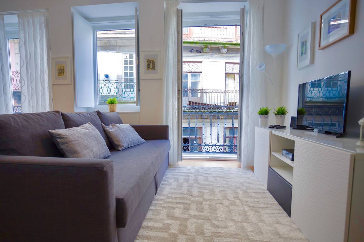 Una sala de estar moderna con sofá, televisor y balcón con barandilla metálica.