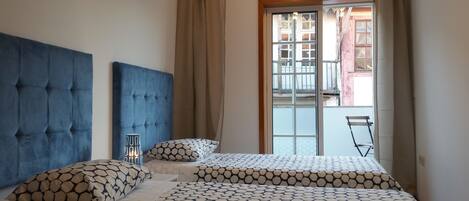 A bedroom with a large bed, two pillows, a bedside table, and a view of the outside balcony.