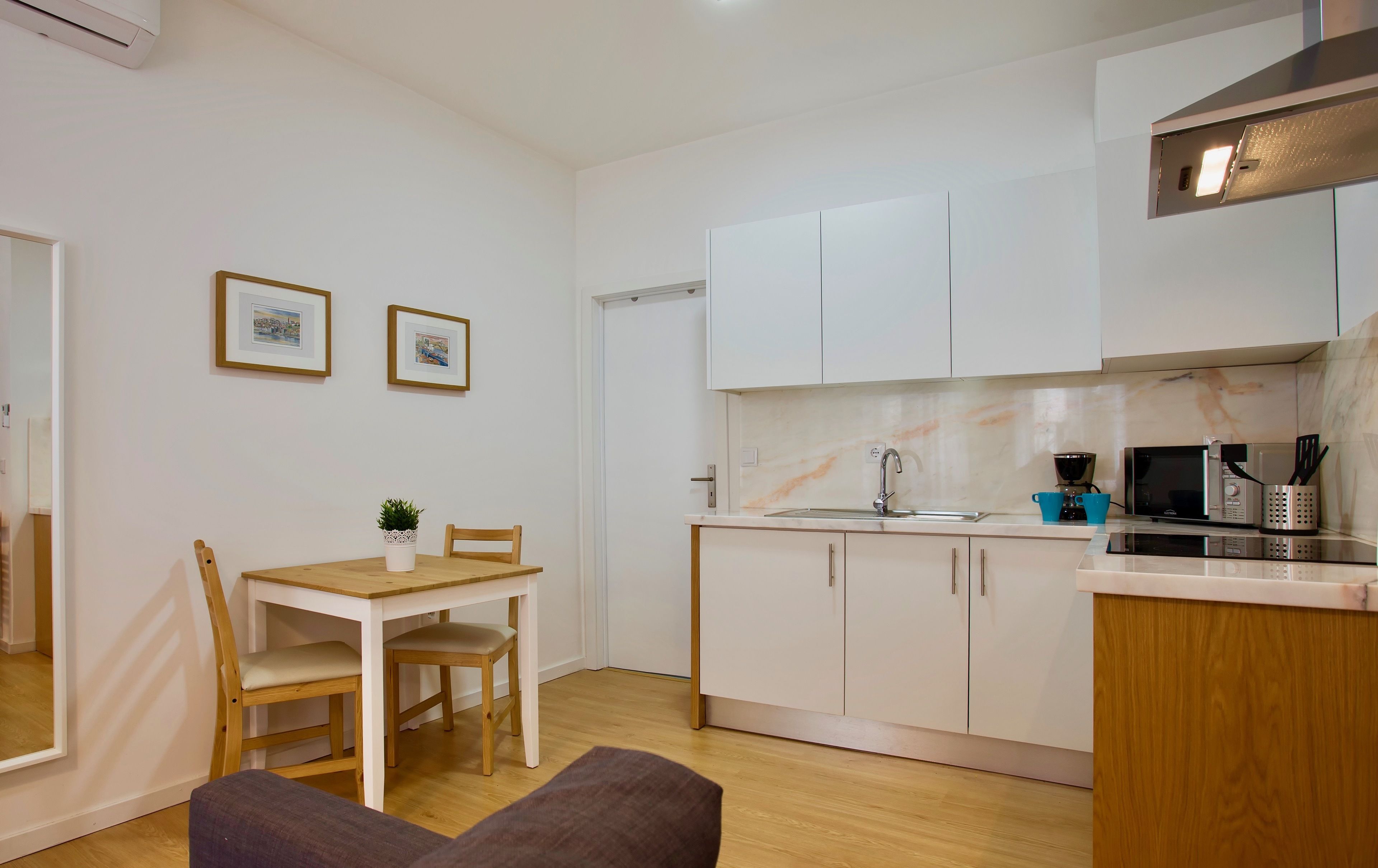 A compact kitchen with white cabinets, a wooden dining table, and a small seating area.