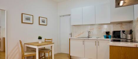 A compact kitchen with white cabinets, a wooden dining table, and a small seating area.