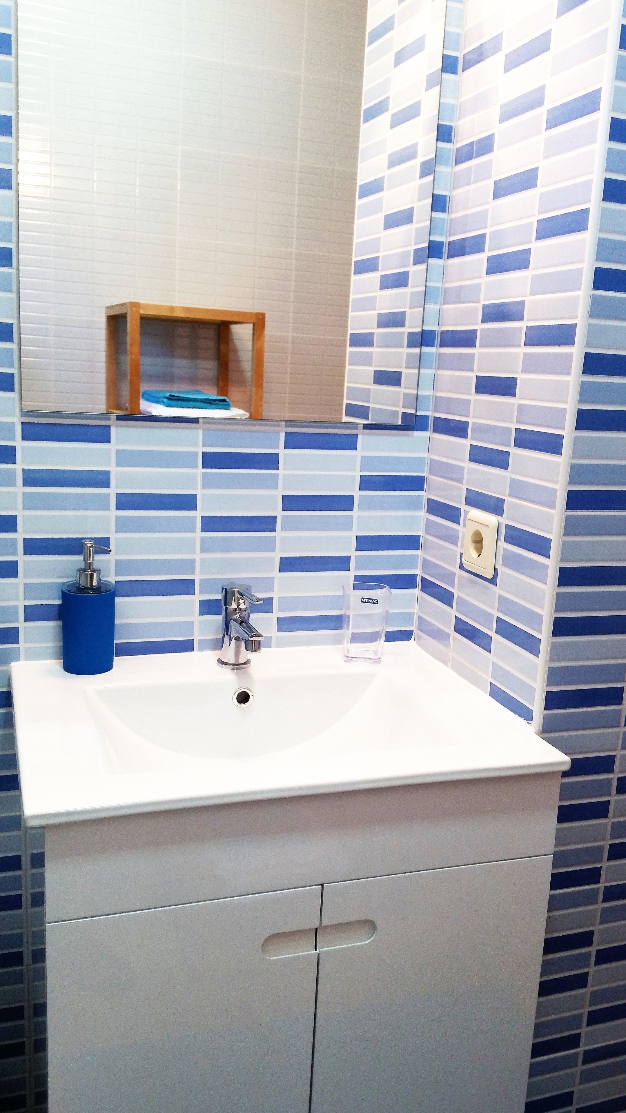 Une salle de bain avec un lavabo blanc, un miroir et des murs recouverts de carreaux bleus et blancs.