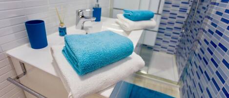 A bathroom with a white sink, blue towels, and a blue-tiled shower area.