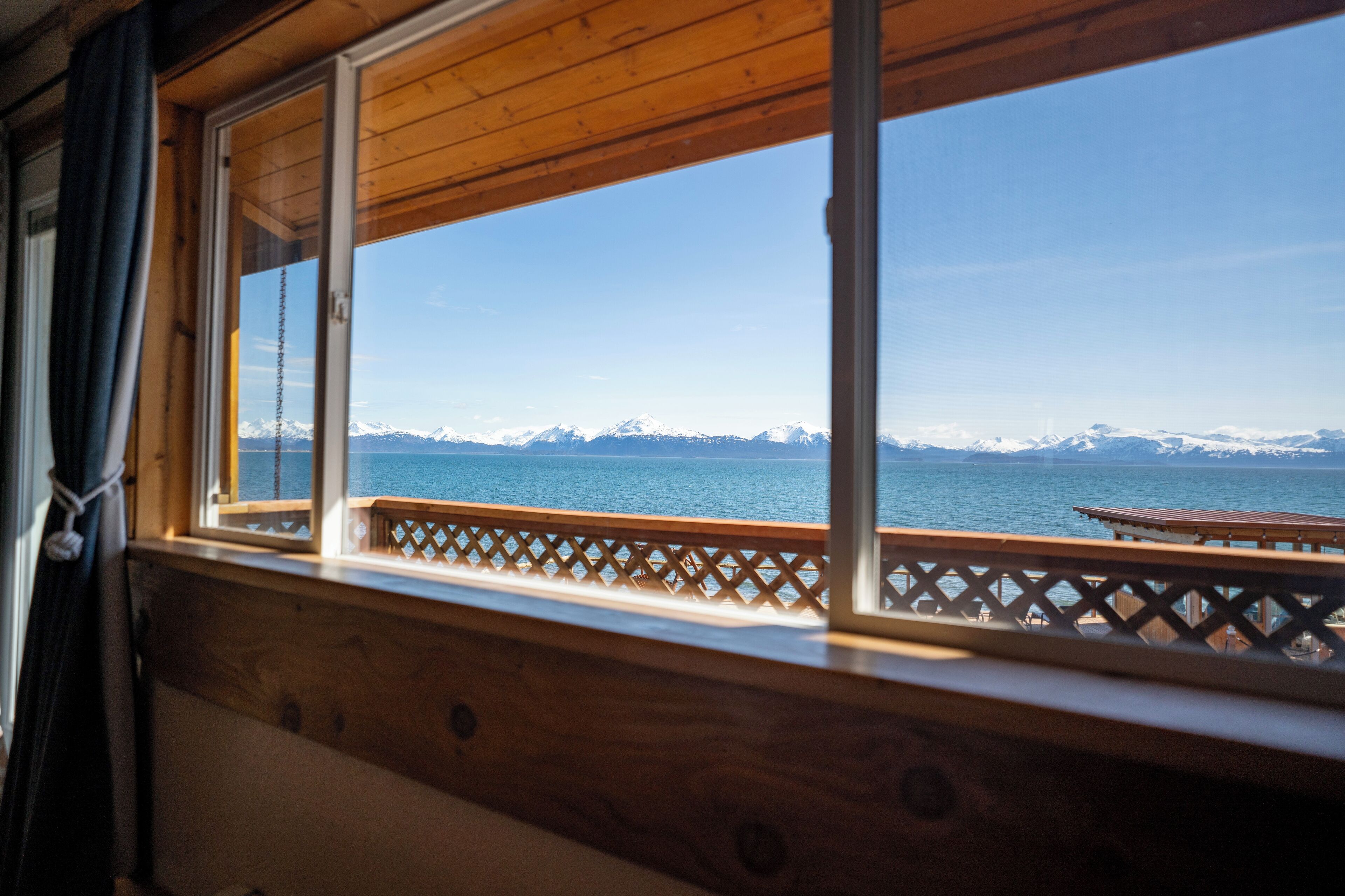 A wooden deck with a view of a calm body of water and snow-capped mountains in the distance.